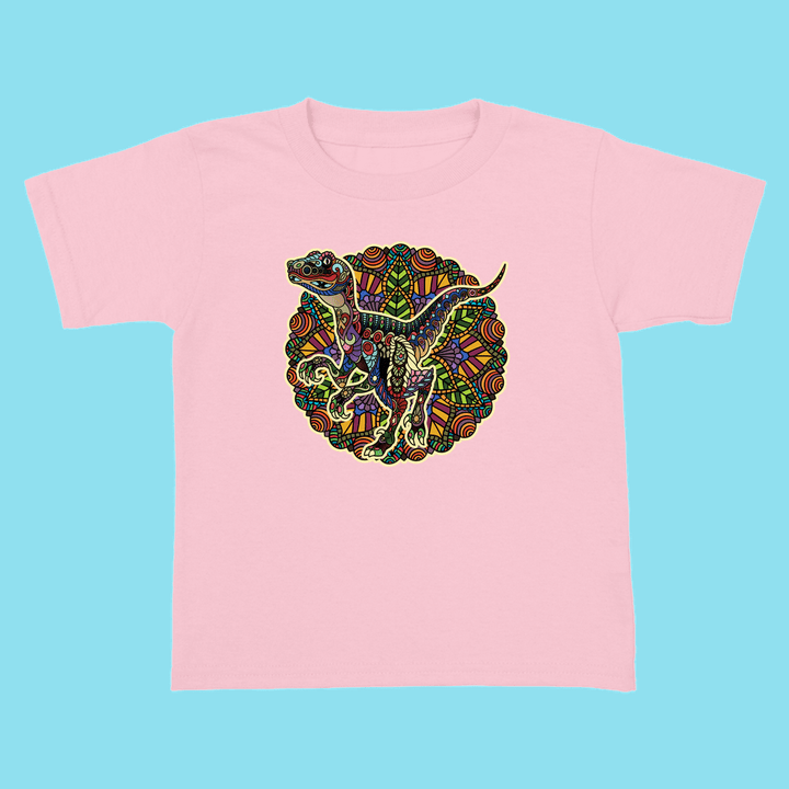 The Toddler Velociraptor Mandala T-Shirt by Jurassic Studio features a colorful, mandala-style dinosaur design on light pink—perfect for any dino fan. Shown on a light blue surface.
