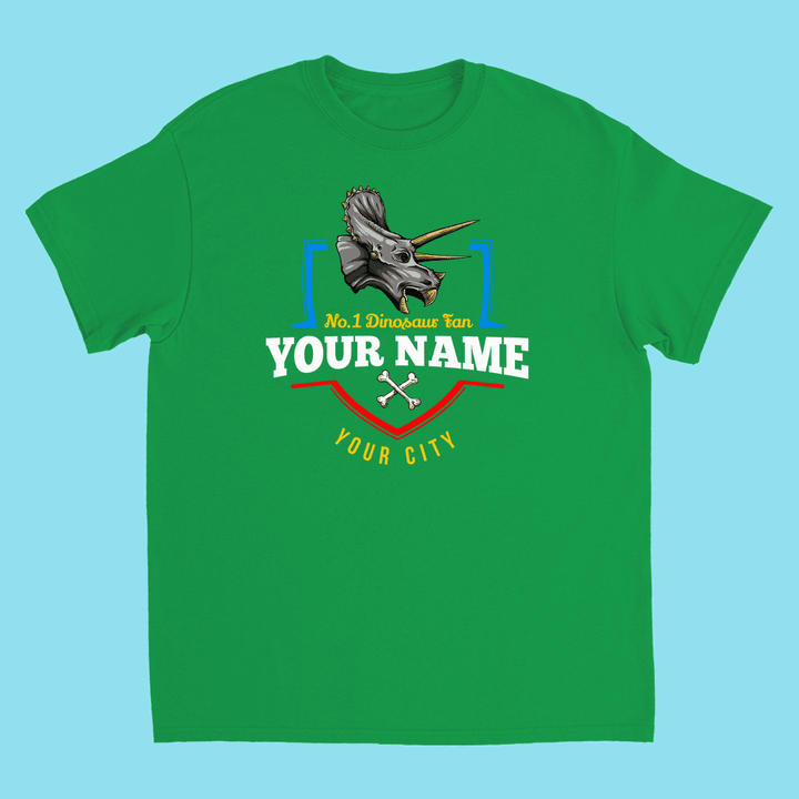 The N.1 Triceratops Fan Custom Kids T-Shirt by Jurassic Studio features a triceratops head, crossed bones, and your custom name/city—ideal as a personalized dinosaur gift for kids. Light blue background.