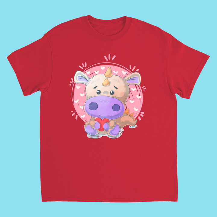The Kids Pink Baby Dino T-Shirt by Jurassic Studio features a cute cartoon dino with a red bow, set in a pink circle with heart motifs on a light blue background.