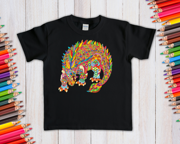 The Kids Ankylosaurus Zentangle T-Shirt by Jurassic Studio features a vibrant patterned dinosaur design, displayed on a light wooden surface with colorful pencils along the edges—a unique and creative choice for dino fans.