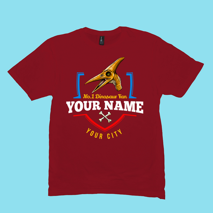 The N.1 Pterodactyl Fan Custom Men T-Shirt by Jurassic Studio features a cartoon dino, No. 1 Dinosaur Fan text, your name and city, plus crossed bones—a unique personalized shirt for dinosaur lovers!.