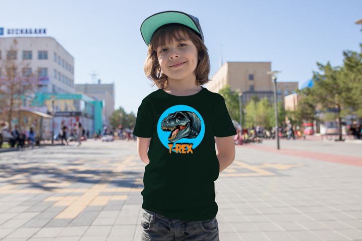 A young child in a black Jurassic Studio Kids T-Rex Head T-Shirt and teal cap stands on a city walkway with people and buildings behind—an ideal gift for any dinosaur fan.