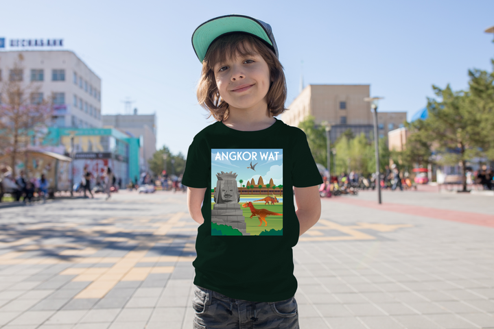 A smiling child wearing a cap and a black Kids Angkor Wat T-Shirt from Jurassic Studio stands in a sunny city square with people and buildings in the background.