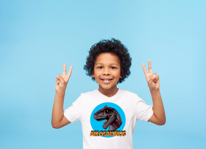 A smiling child in a white Kids Allosaurus Head T-Shirt by Jurassic Studio flashes peace signs against a light blue background. The perfect gift for dinosaur fans!.