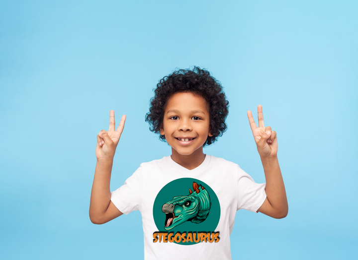 A smiling child with curly hair, wearing a white Jurassic Studio Kids Stegosaurus Head T-Shirt featuring a cartoon stegosaurus and “STEGOSAURUS” text, flashes peace signs against a plain light blue background—a perfect dinosaur fan gift.