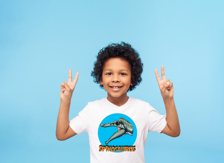 A smiling child wearing the Kids Spinosaurus Head T-Shirt from Jurassic Studio flashes peace signs with both hands against a solid light blue background.