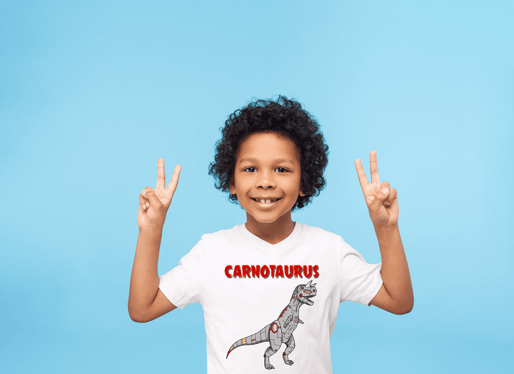A smiling, curly-haired child wears the Jurassic Studio Kids Robot Carnotaurus T-Shirt with a cartoon dinosaur, flashing peace signs against a bright blue background—the perfect gift for young dinosaur fans.