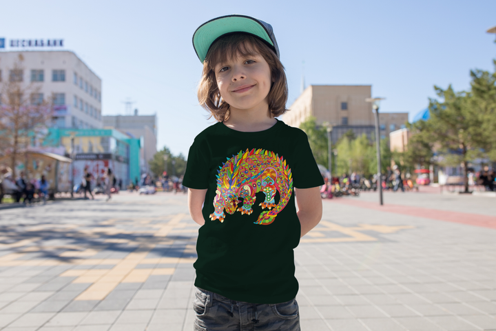 A smiling child wears the Kids Ankylosaurus Zentangle T-Shirt by Jurassic Studio, featuring a vibrant dinosaur design—an ideal gift for young dino fans—while outdoors on a sunny day with softly blurred buildings and people behind.