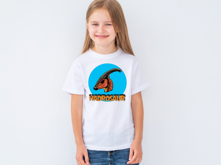 Smiling young girl wears the Kids Hadrosaur Head T-Shirt by Jurassic Studio, featuring an illustrated hadrosaur head in a blue circle—perfect gift for dinosaur fans!.