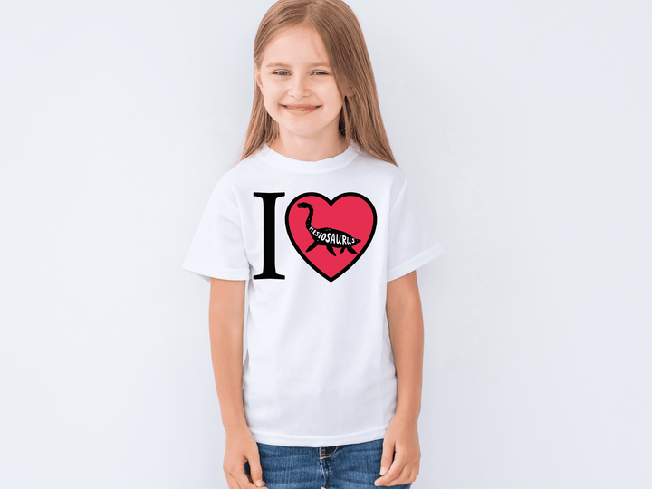 Smiling young girl wears the Kids I Love Plesiosaurus T-Shirt by Jurassic Studio, featuring I ♥ Dinosaurs with a dinosaur-shaped heart and “DINOSAURS” inside. A cute gift for dino fans, shown on a plain white background.