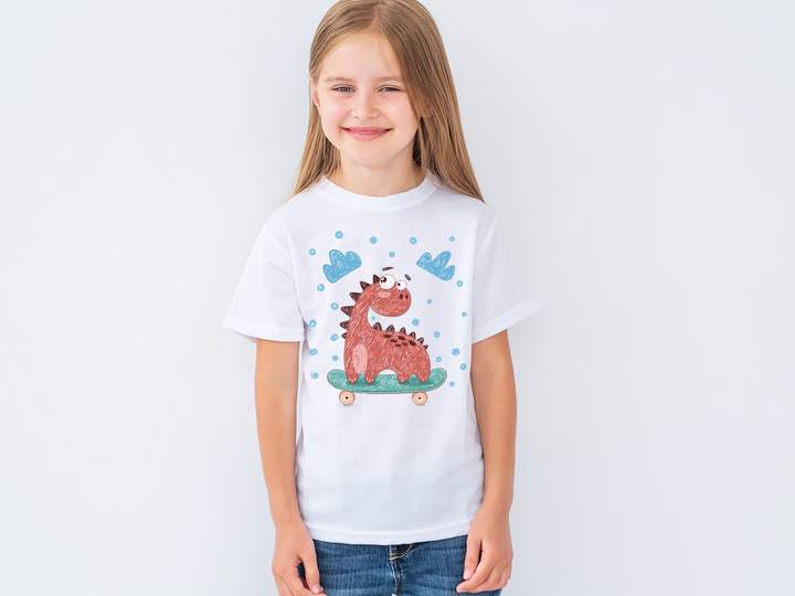 A smiling young girl with long blonde hair wears the Jurassic Studio Kids Baby Dino Skate T-Shirt, featuring a cartoon red dinosaur on a skateboard with blue clouds and dots, standing against a plain white background.