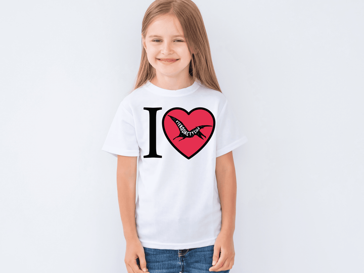 A smiling young girl wears the Kids I Love Pterodactyl T-Shirt by Jurassic Studio against a plain light background—a fun choice for little dino fans.