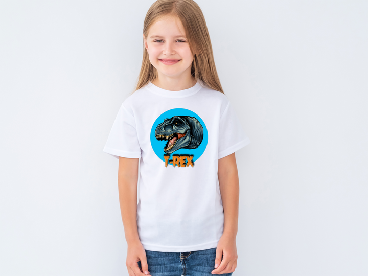 A young girl with long blonde hair smiles against a light background, wearing the Jurassic Studio Kids T-Rex Head T-Shirt featuring a roaring dinosaur in a blue circle—an ideal gift for any dino fan.