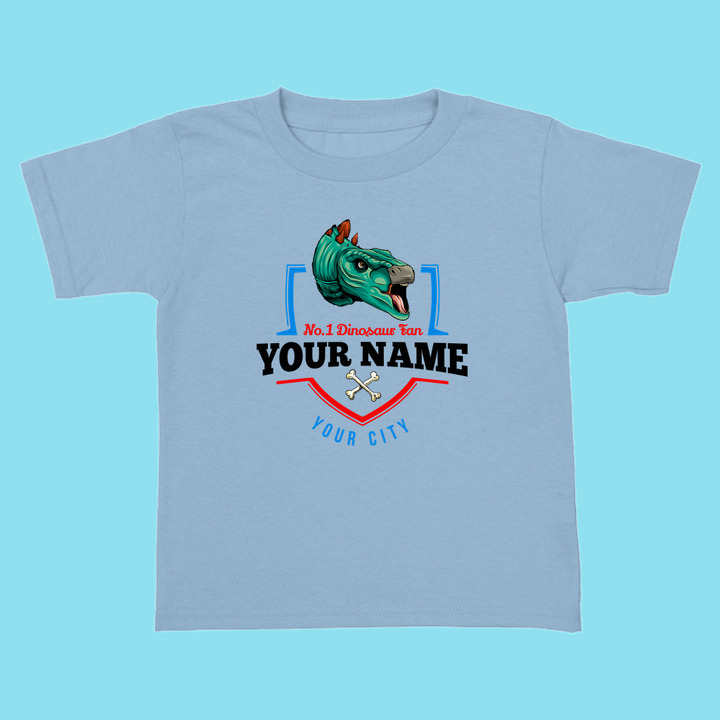 The N.1 Stegosaurus Fan Custom Toddler T-Shirt by Jurassic Studio is a light blue shirt for kids, featuring a cartoon stegosaurus, crossed bones, and personalized with your childs name and city—a cute dinosaur gift.