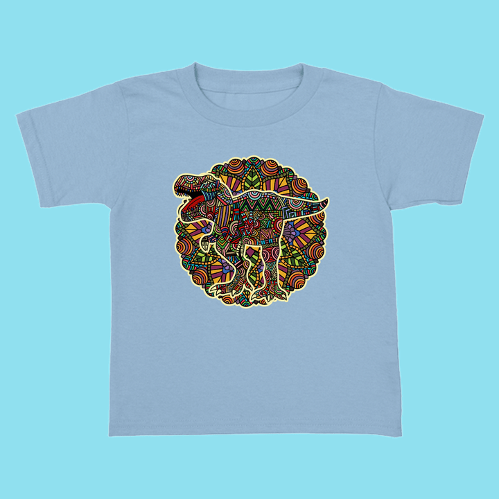 The Jurassic Studio Toddler T-Rex Mandala T-Shirt is light blue, 100% cotton, and showcases a vibrant tribal mosaic dinosaur design—perfect for young dinosaur fans.