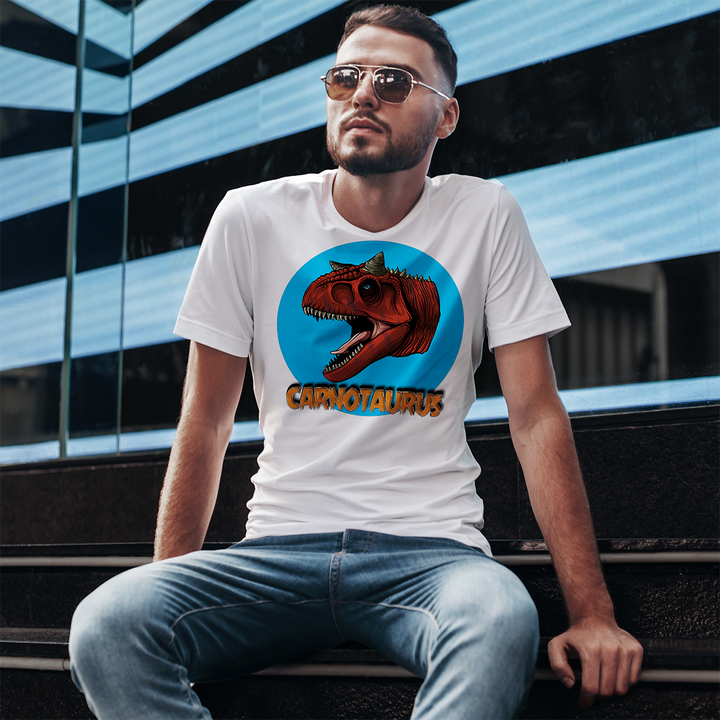A bearded man in sunglasses and jeans sits on steps wearing the Men Carnotaurus Head T-Shirt by Jurassic Studio—an exclusive dinosaur fan gift with a roaring red Carnotaurus in a blue circle and bold orange CARNOTAURUS text.