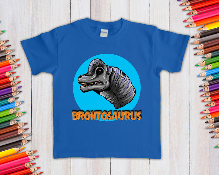 The Kids Brontosaurus Head T-Shirt by Jurassic Studio features a cartoon dinosaur head on blue with “BRONTOSAURUS” in bold orange below—a fun, exclusive gift for young dino fans, shown alongside colorful pencils.