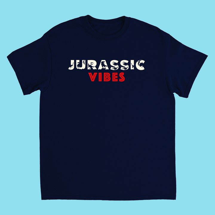 The Kids Jurassic Vibes T-Shirt by Jurassic Studio features JURASSIC in white fossil-style and VIBES in bold red on navy blue, against a light blue background. Made from 100% cotton—ideal for dinosaur fans.