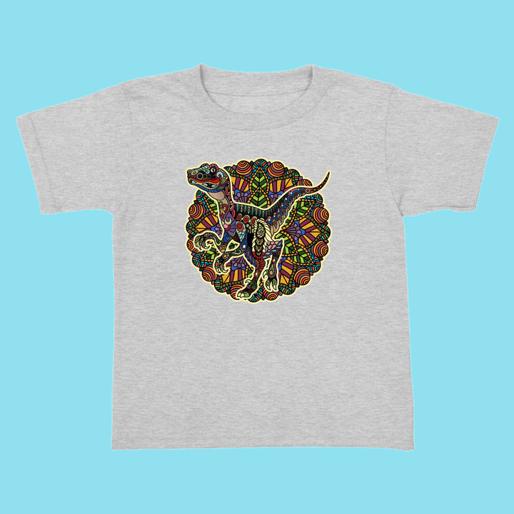 The Jurassic Studio Toddler Velociraptor Mandala T-Shirt features a gray design with a colorful, abstract dinosaur illustration—perfect for little dinosaur fans and available exclusively from Jurassic Studio.