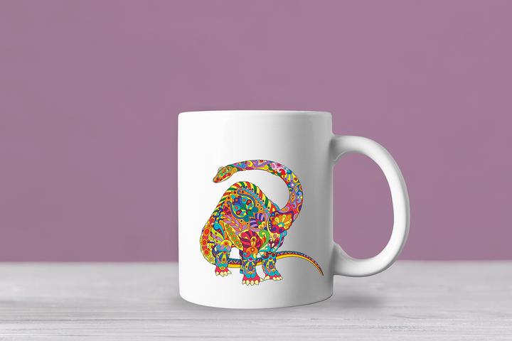 The Jurassic Studio Brontosaurus Zentangle Mug is a white ceramic coffee mug with a vibrant floral-patterned dinosaur design set against a light purple background, displayed on a white wooden surface.