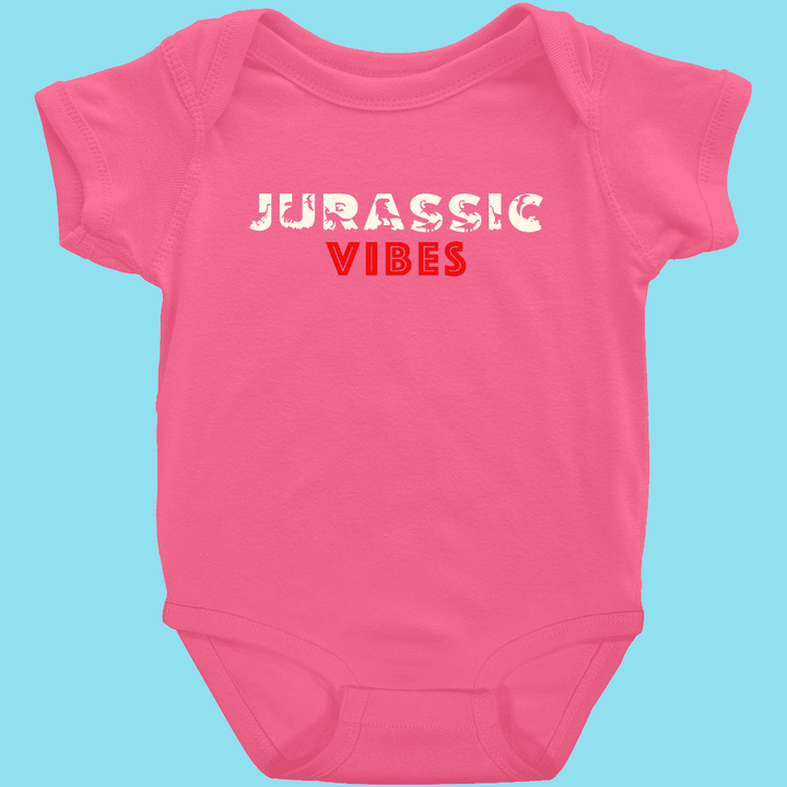 The Toddler Jurassic Vibes Onesie by Jurassic Studio is a pink 100% cotton bodysuit with JURASSIC VIBES—distressed white JURASSIC and bold red VIBES—on the chest, standing out against a light blue background.