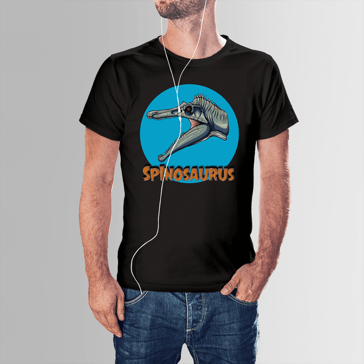 A man in the Men Spinosaurus Head T-Shirt by Jurassic Studio, featuring an illustrated Spinosaurus head in a blue circle with SPINOSAURUS in orange—an exclusive gift for dinosaur fans—stands with one hand in his pocket and wears headphones.