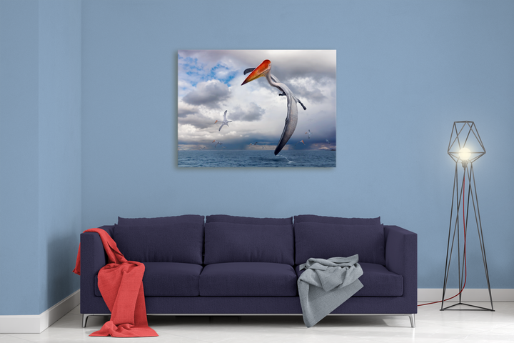 A modern living room showcases a dark blue sofa, red and gray blankets, a unique floor lamp, and above the sofa, the Jurassic Studio “Azhdarcho Flying Canvas Wrap,” depicting a seabird catching a fish over an ocean beneath cloudy skies.