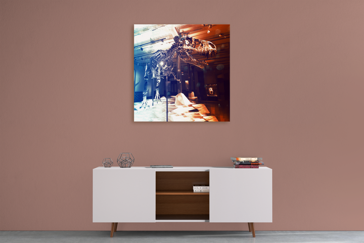 A minimalist sideboard with books and decor sits against a mauve wall, topped by Jurassic Studios T-Rex Full Skeleton Canvas Wrap—a striking artwork that showcases the dinosaur skeleton in contrasting cool and warm tones.