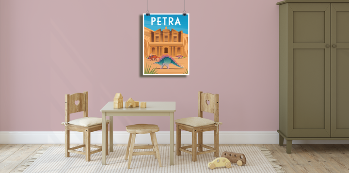A children’s playroom features a small table, two wooden chairs, toys on a rug, a green wardrobe, and the colorful Petra Poster by Jurassic Studio with camels, a peacock, and dinosaurs hanging on the pink wall above the table.