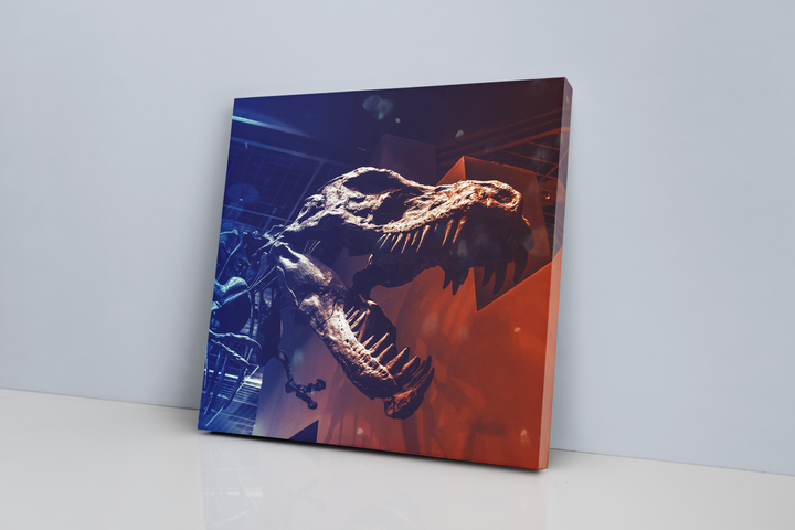 The Jurassic Studio T-Rex Skeleton Canvas Wrap features dynamic blue and orange lighting on a striking T. rex skull close-up, displayed against a white wall—an ideal decor piece for fans of unique dinosaur art.