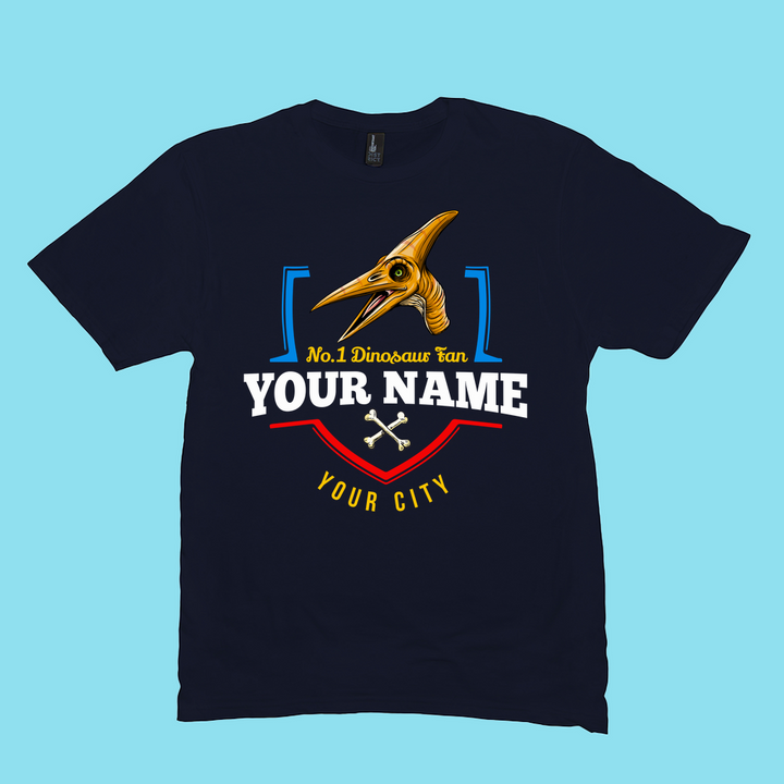 Personalize your N.1 Pterodactyl Fan Custom Men T-Shirt from Jurassic Studio, featuring a cartoon dino, crossed bones, and No.1 Dinosaur fan YOUR NAME and YOUR CITY on a light blue background. The perfect gift for dino lovers!.