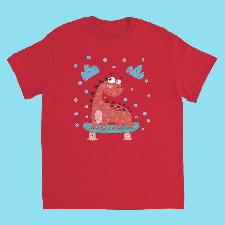 The Jurassic Studio Kids Baby Dino Skate T-Shirt features a cute cartoon dinosaur skateboarding with blue clouds and dots on a light blue background.
