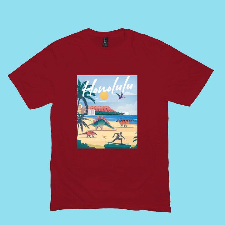 The Men Honolulu T-Shirt by Jurassic Studio is a 100% cotton red shirt featuring an illustrated beach scene with palm trees, surfers, swimmers, and Honolulu in white script set against a blue sky and ocean backdrop.
