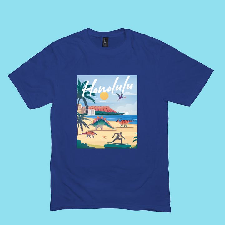 The Men Honolulu T-Shirt by Jurassic Studio is 100% cotton, with a vibrant beach scene—palm trees, surfers, mountains, sunny sky—and “Honolulu” in white script at the top.