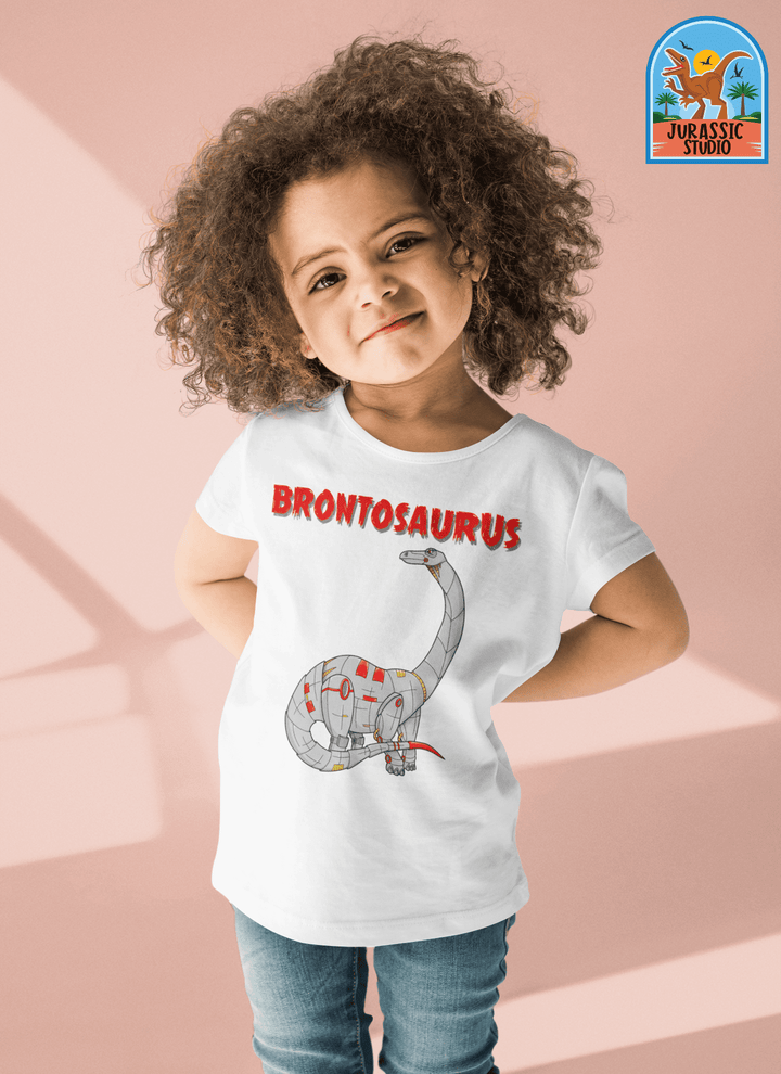 A young child smiles in a Toddler Robot Brontosaurus T-Shirt by Jurassic Studio, featuring a cartoon robot brontosaurus and red BRONTOSAURUS text. The exclusive Jurassic Studio logo appears in the top right corner.