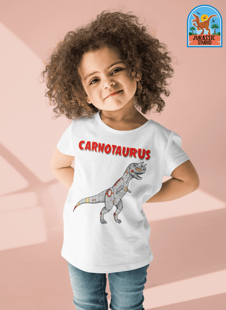 A smiling young child wears the Jurassic Studio Toddler Robot Carnotaurus T-Shirt, featuring a cartoon robot Carnotaurus and bold red CARNOTAURUS text—perfect for dino fans. The Jurassic Studio logo is in the upper right corner.