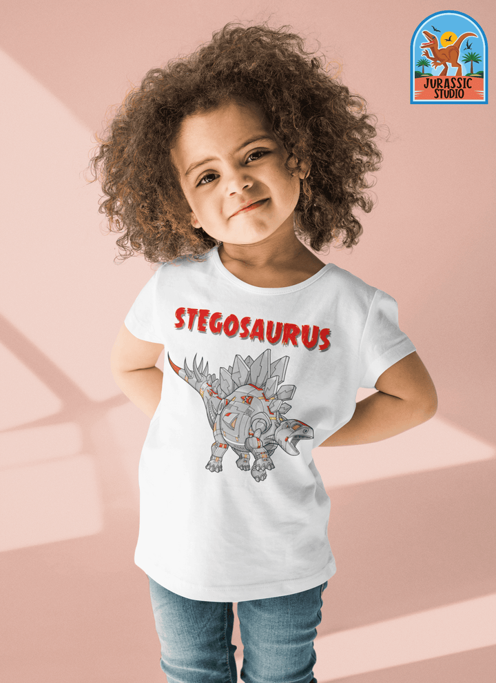 A smiling child in the Jurassic Studio Toddler Robot Stegosaurus T-Shirt—a great gift for dinosaur fans—shows off a cartoon stegosaurus and bold red “STEGOSAURUS” text on pale pink.