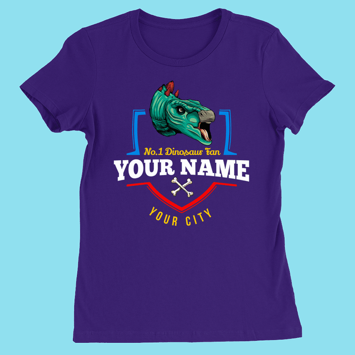 Jurassic Studio N.1 Stegosaurus Fan Custom Women T-Shirt: purple slim fit with a blue and green dinosaur head, crossed bones, and bold customizable text “N.1 Dinosaur Fan YOUR NAME YOUR CITY” on a light blue background.