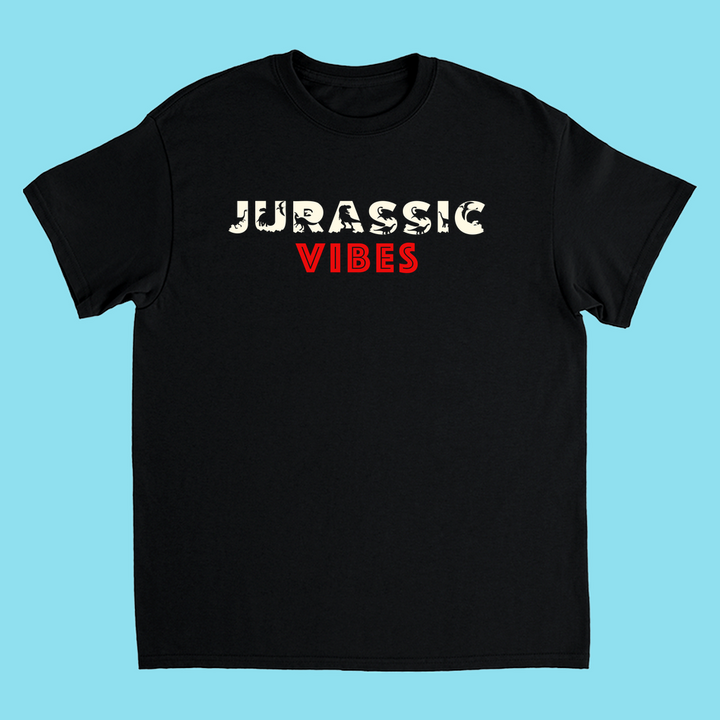 The Kids Jurassic Vibes T-Shirt by Jurassic Studio features JURASSIC in bold fossil-textured off-white and VIBES in bold red on black, 100% cotton—ideal for dinosaur fans. Shown on a light blue background.
