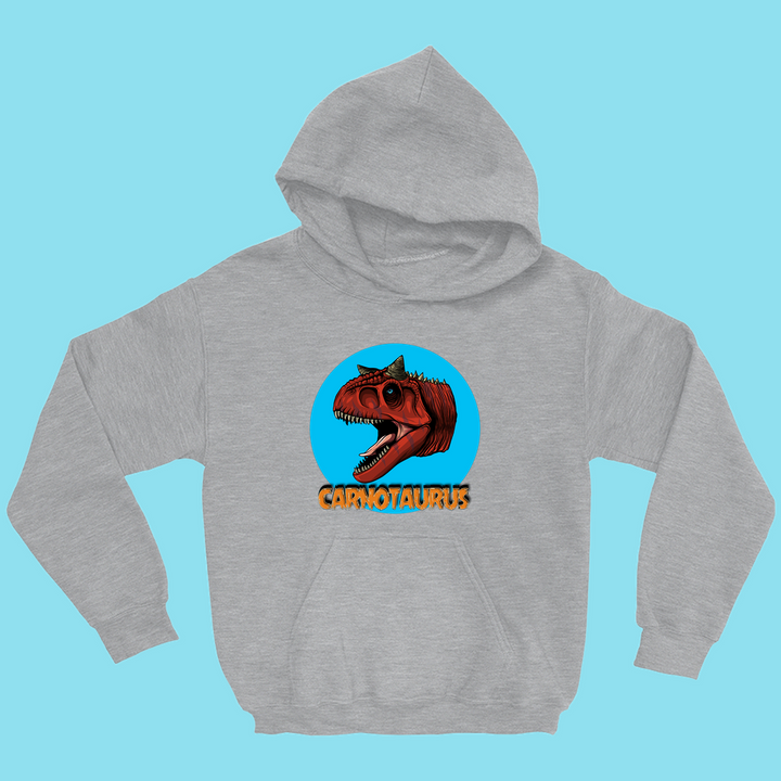 The Jurassic Studio Kids Carnotaurus Head Hoodie features a red Carnotaurus graphic in a blue circle above bold yellow text on a light blue background. This exclusive hoodie is perfect for young dinosaur fans.