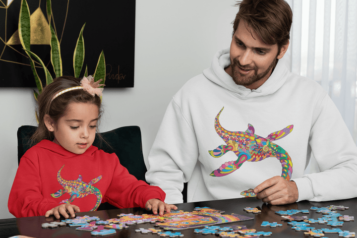 A man in a white Jurassic Studio Men Plesiosaurus Zentangle Hoodie and a girl in a red hoodie work together on a jigsaw puzzle, both focused at the table.