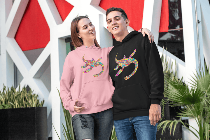 A smiling couple stands outdoors in Jurassic Studio hoodies with colorful abstract lizard designs; she wears a pink hoodie and he wears the black Men Plesiosaurus Zentangle Hoodie, with a modern building and greenery behind them.