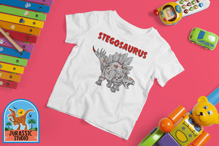 The Jurassic Studio Toddler Robot Stegosaurus T-Shirt features a white tee with a cartoon robotic stegosaurus and red STEGOSAURUS print, surrounded by colorful toys—an ideal gift for dinosaur fans—displayed on a pink background.