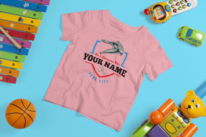 The N.1 Spinosaurus Fan Custom Toddler T-Shirt by Jurassic Studio features a cute dino design with your child’s name and city, plus playful toys—xylophone, toy phone, car, basketball, teddy bear—making it a perfect dinosaur gift for toddlers.