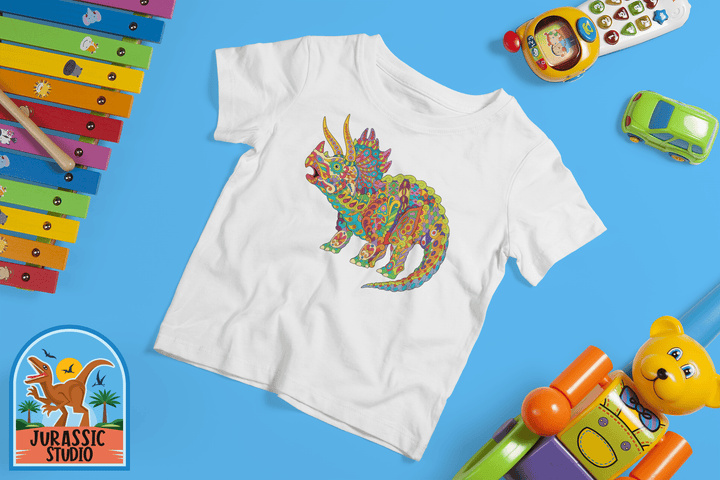 Jurassic Studio’s Toddler Triceratops Zentangle T-Shirt showcases a colorful dinosaur with toys on a blue background—perfect for young dino fans. The Jurassic Studio logo appears at the lower left.