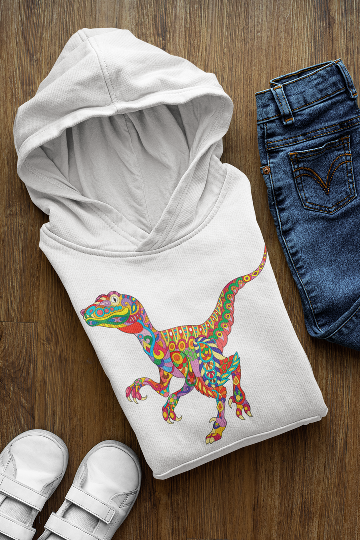 A folded Jurassic Studio Kids Velociraptor Zentangle Hoodie with a colorful dinosaur graphic is placed next to blue jeans and white shoes on a wooden floor.