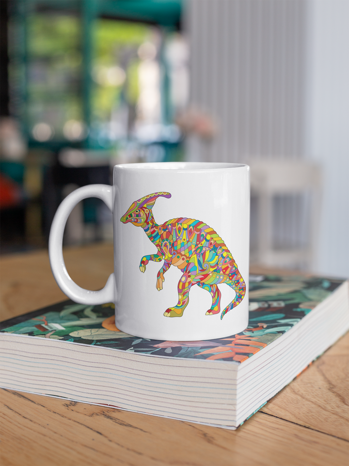 The Hadrosaur Zentangle Mug by Jurassic Studio, a white ceramic mug with exclusive dinosaur art, rests on a closed book atop a wooden table in a bright, modern café.