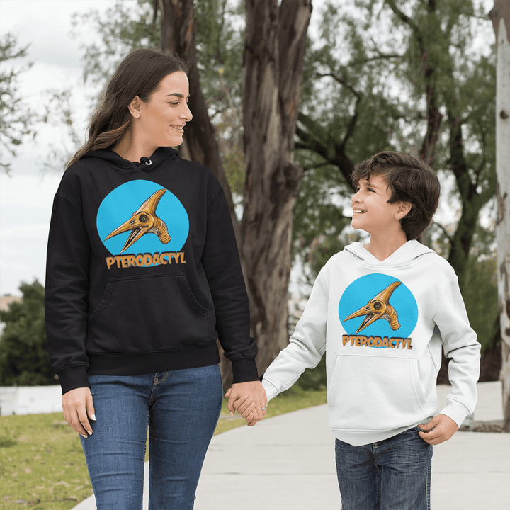 A woman and boy stroll outdoors, smiling in Jurassic Studio unisex hoodies with a pterodactyl graphic—the perfect dinosaur fan gift. She wears the Women Pterodactyl Head Hoodie in black; his is white. Trees and a path appear behind them.