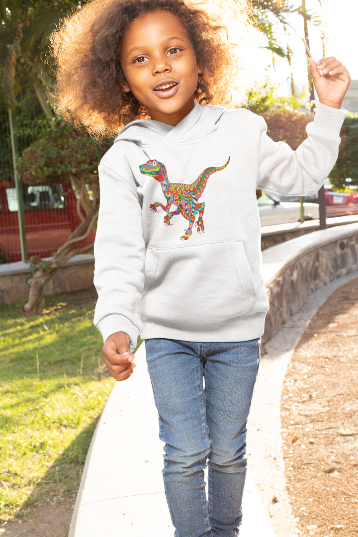 A smiling child with curly hair walks outdoors in a Jurassic Studio Kids Velociraptor Zentangle Hoodie, featuring a vibrant dinosaur design, paired with blue jeans. Sunlight and greenery brighten the background.