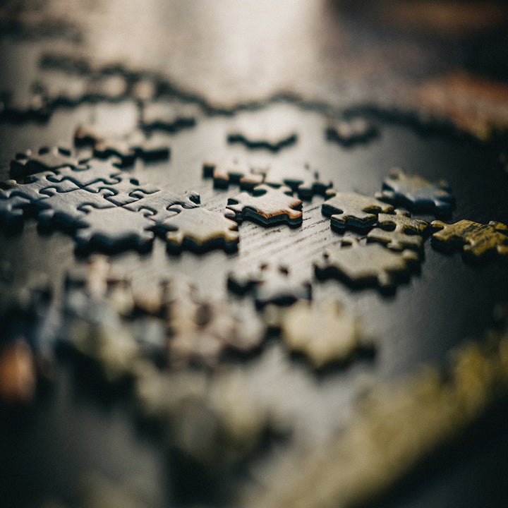 Close-up of several interlocking Rio de Janeiro Puzzle pieces by Jurassic Studio, some connected and others scattered on a dark, textured surface. The softly focused shot creates a warm, inviting atmosphere for this family indoor game.
